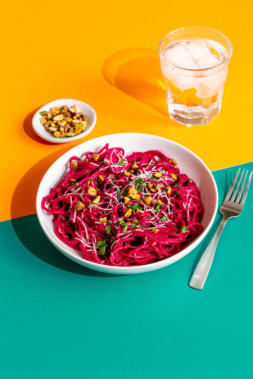Bowl of pink pasta with chickpeas on a yellow and blue background