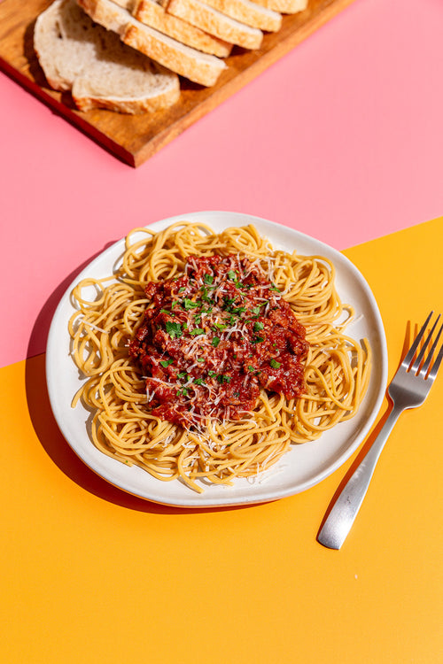 Plate of spaghetti with tomato sauce on a pink and yellow background