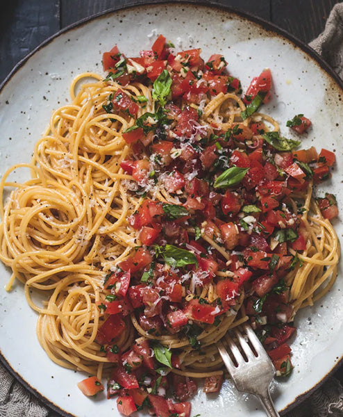 Spaghetti with tomato and basil salad on a speckled plate