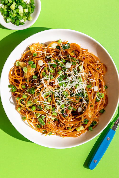 Spaghetti dish with green onions and parmesan on a white plate against a green background