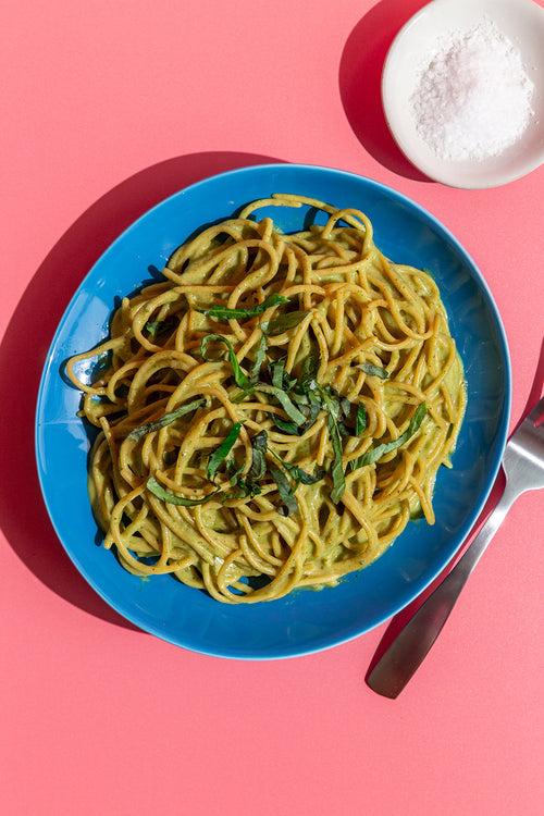 Blue plate with spaghetti and greens on a pink background
