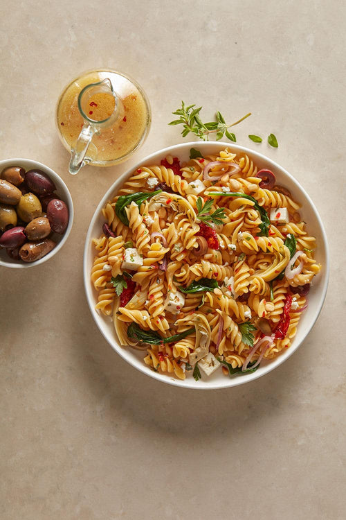 Pasta salad with vegetables and a glass of white wine on a beige surface