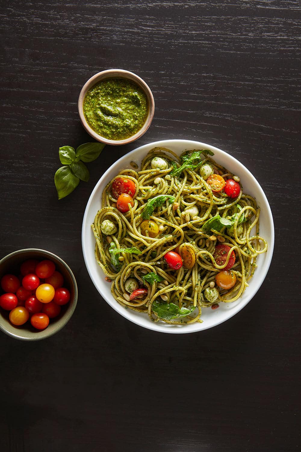 Bowl of pasta with vegetables and pesto on a dark surface