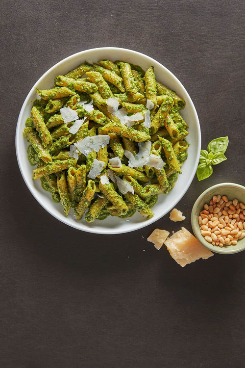 Green pasta dish with parmesan in a white bowl on a dark surface