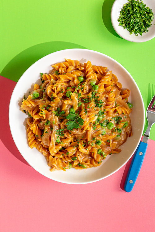 Pasta dish with green peas and herbs in a white bowl on a colorful background