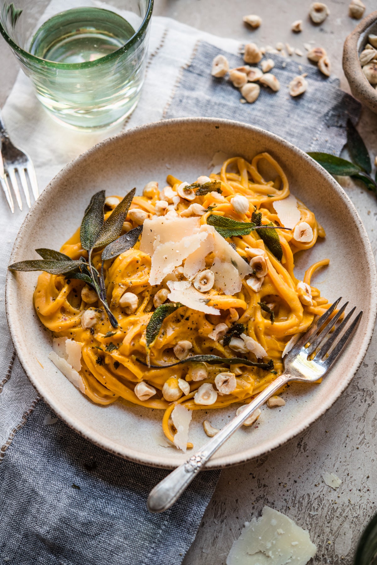 Plate of pumpkin pasta with sage and parmesan on a rustic table setting.