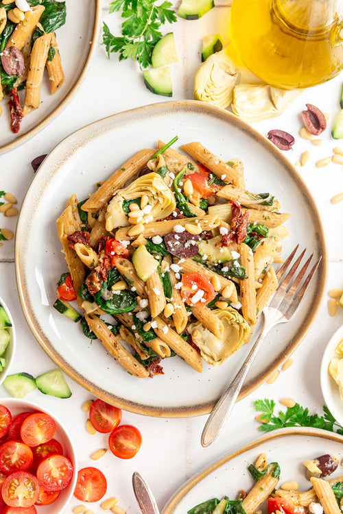 Pasta dish with vegetables on a white plate with a fork, surrounded by ingredients.