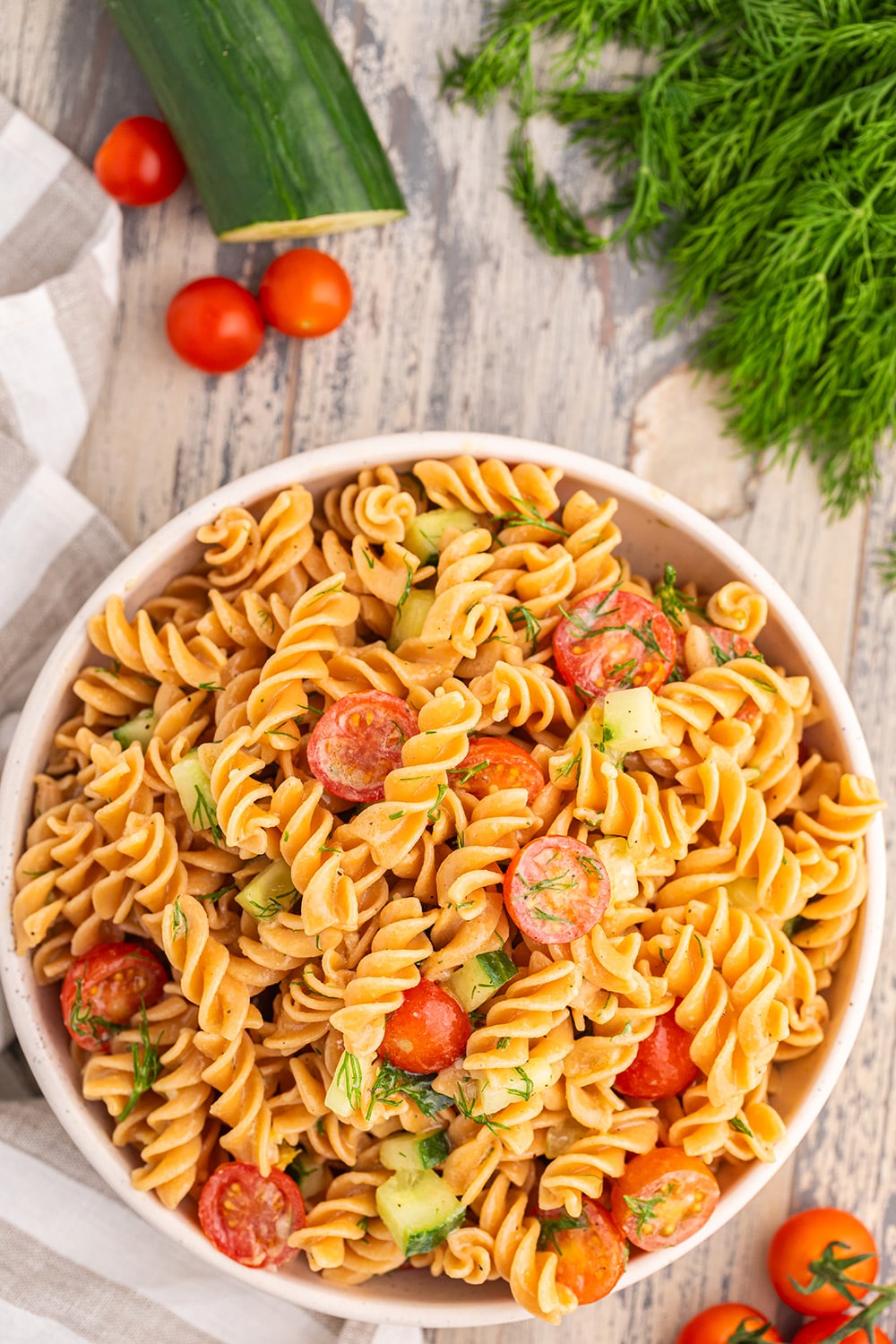 Pasta salad with tomatoes and cucumbers in a bowl on a wooden surface