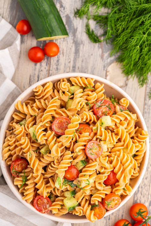 Pasta salad with tomatoes and cucumbers in a bowl on a wooden surface