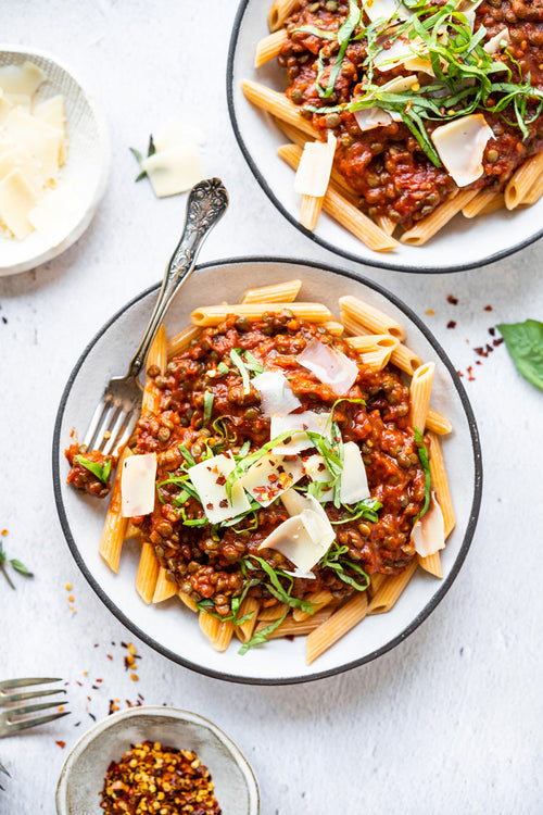 Two bowls of pasta with a meat sauce, garnished with parmesan cheese, on a light surface.