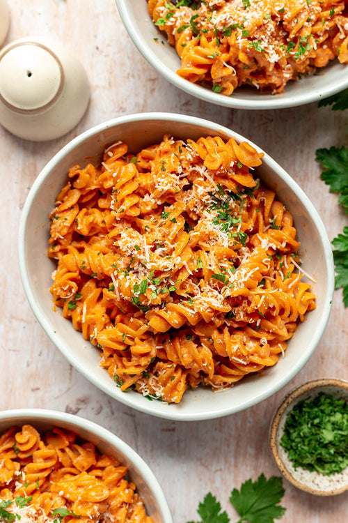Bowls of red pasta with parmesan cheese on a light background