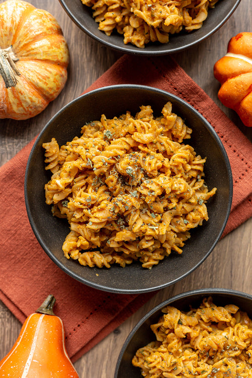 Bowls of pumpkin pasta with pumpkins on a wooden surface