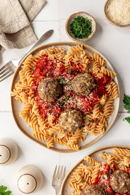 Plate of pasta with meatballs on a white table with ingredients around