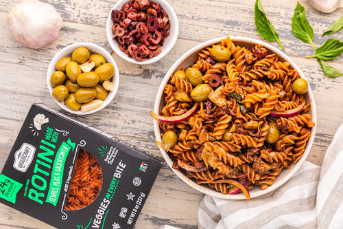 Pasta dish with olives and dried tomatoes on a wooden table, featuring a package of Rotini brand pasta.