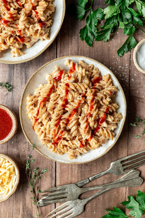 Plates of pasta with red sauce on a wooden table with herbs and forks.