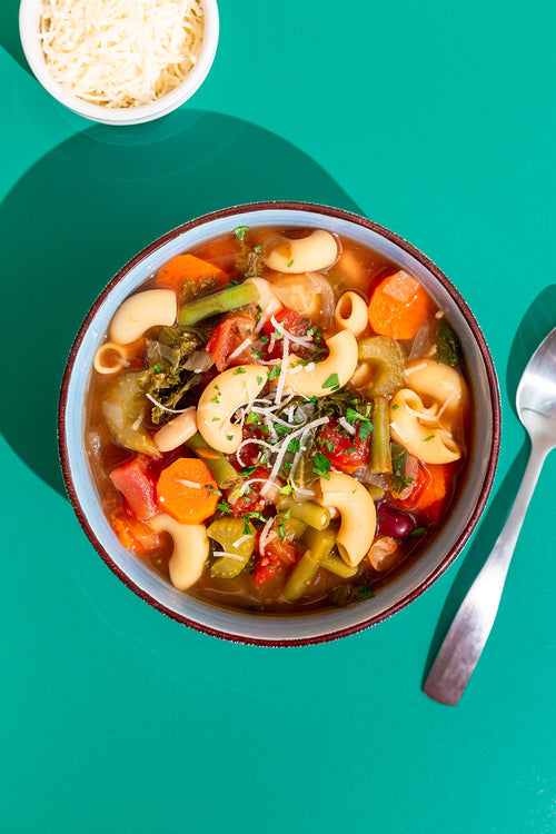 Bowl of vegetable soup with pasta on a teal background