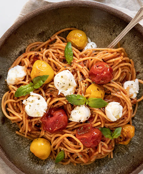 Spaghetti dish with cherry tomatoes and mozzarella pearls on a textured plate.