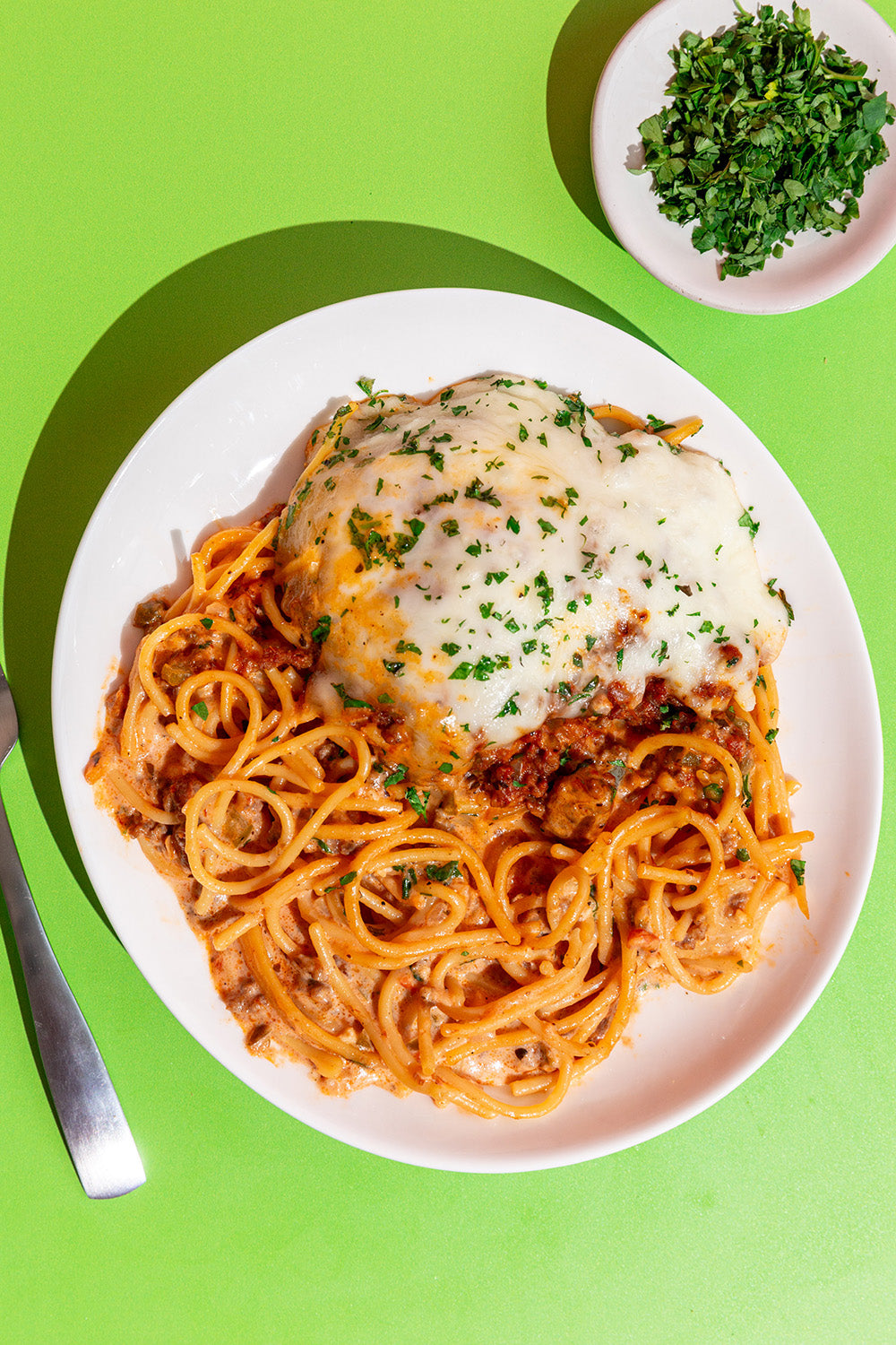 Spaghetti dish with cheese on a white plate against a green background