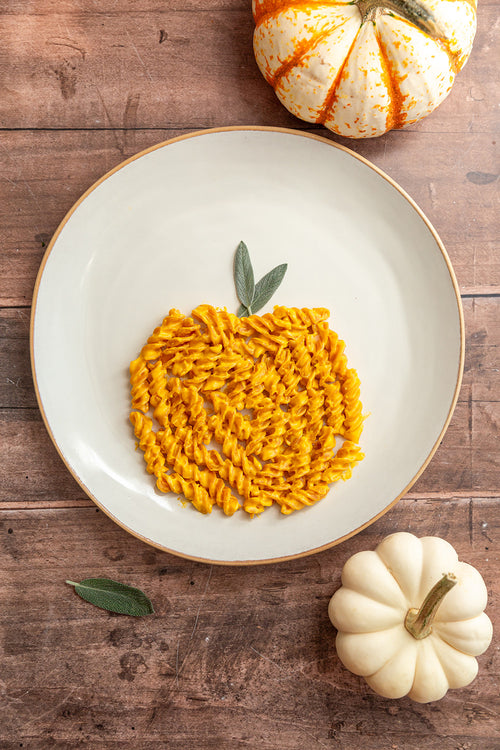 Pumpkin-shaped pasta on a plate with small pumpkins on a wooden surface