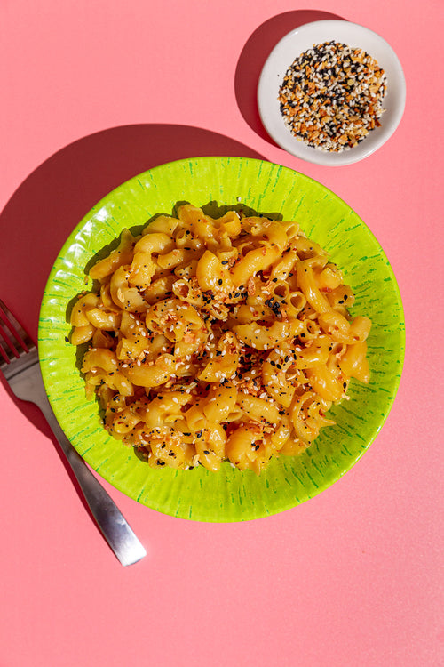 Macaroni and cheese on a green plate with a side of everything bagel seasoning on a pink background