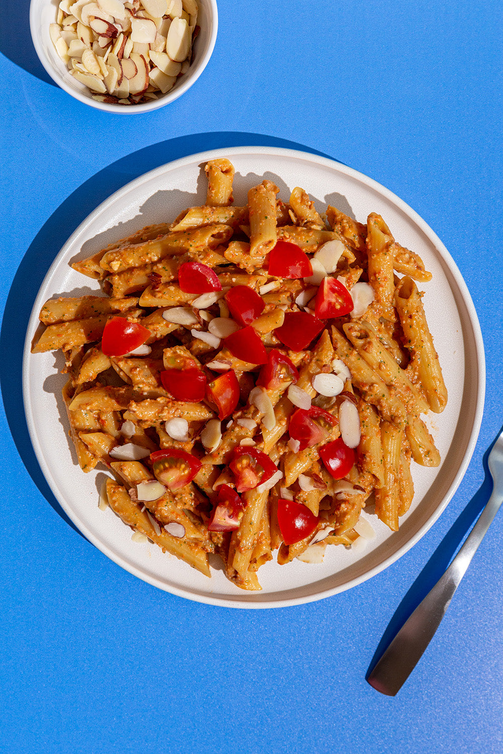 Plate of penne pasta with cherry tomatoes and cashews on a blue background