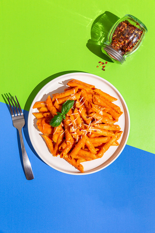 Plate of penne pasta with red sauce on a blue and green background