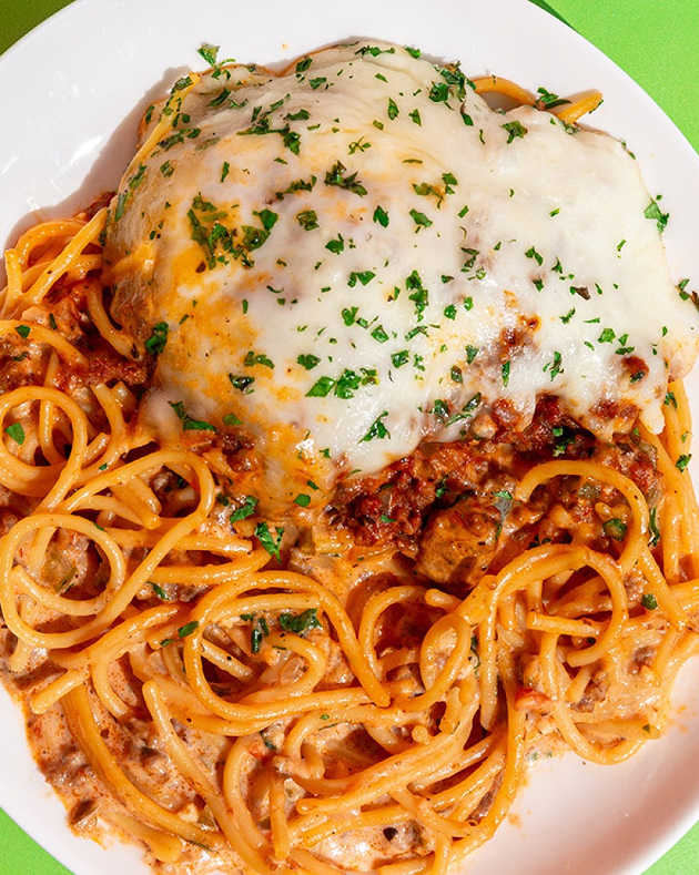 Spaghetti with meat sauce and melted cheese on a white plate with a green background