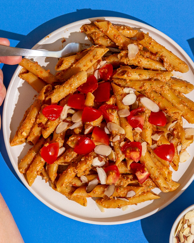 Penne pasta with cherry tomatoes and almonds on a white plate against a blue background